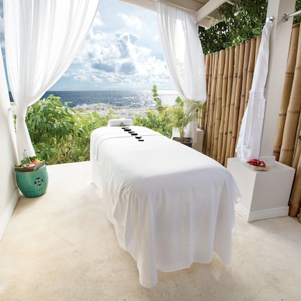 A spa room with a massage table, a view of the ocean, and a bamboo fence.