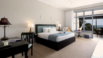 Una habitación de hotel moderna con una cama grande, dos mesitas de noche, un escritorio y vistas al océano.