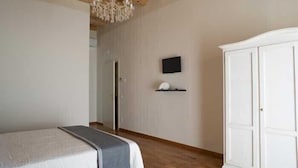 Une chambre à coucher avec un lit, une armoire, un téléviseur fixé au mur et un lustre.