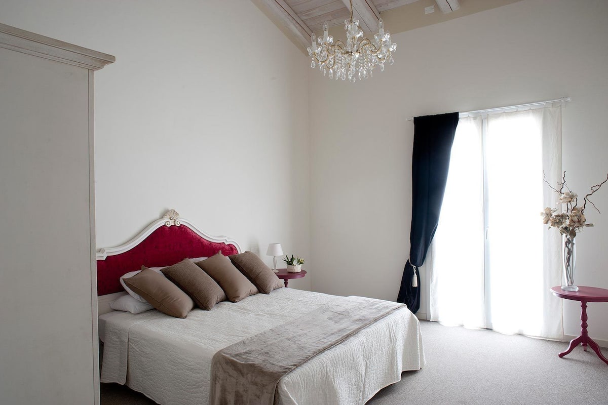 Un dormitorio con cama, un candelabro, una ventana con cortinas y un jarrón con flores.