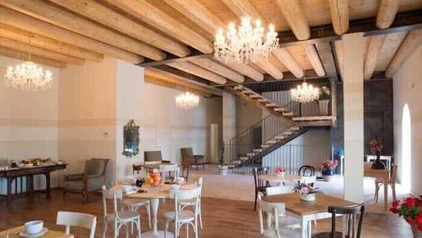 Une salle à manger spacieuse avec des poutres en bois, des chaises blanches et des lustres.