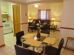 A dining area with a glass table and chairs, a sofa set, and a kitchen in the background. - SoBe Apartments (Miami Beach)