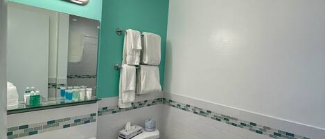 A bathroom with a white sink, a toilet, and a mirror with lights. There are towels hanging on the wall and a small shelf with toiletries.