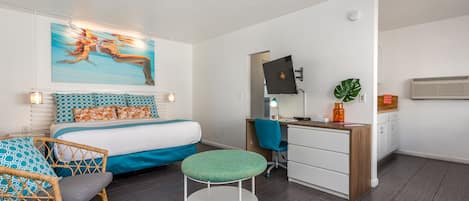 Une chambre d’hôtel moderne, équipée d’un lit, d’un bureau, d’une chaise, d’un petit tabouret, d’un tableau et d’une plante.