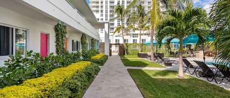 A pathway leading to a pool area with lounge chairs and palm trees.
