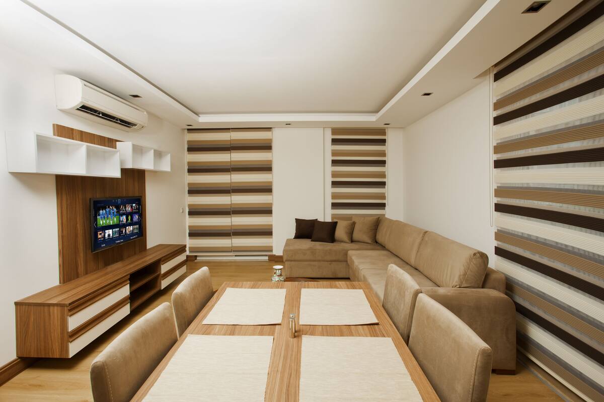Uma sala de estar moderna com um sofá seccional, uma mesa de centro de madeira e uma TV de tela plana presa a um armário de madeira.