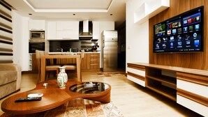 A modern kitchen with a built-in TV, wooden cabinets, and a dining area with a unique guitar-shaped coffee table. - Lara Orkide Homes (Antalya)