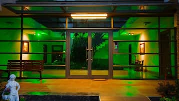 Ein modernes Gebäude mit Glasfassade, einem zentralen Eingang mit Doppeltüren und einer Bank davor.