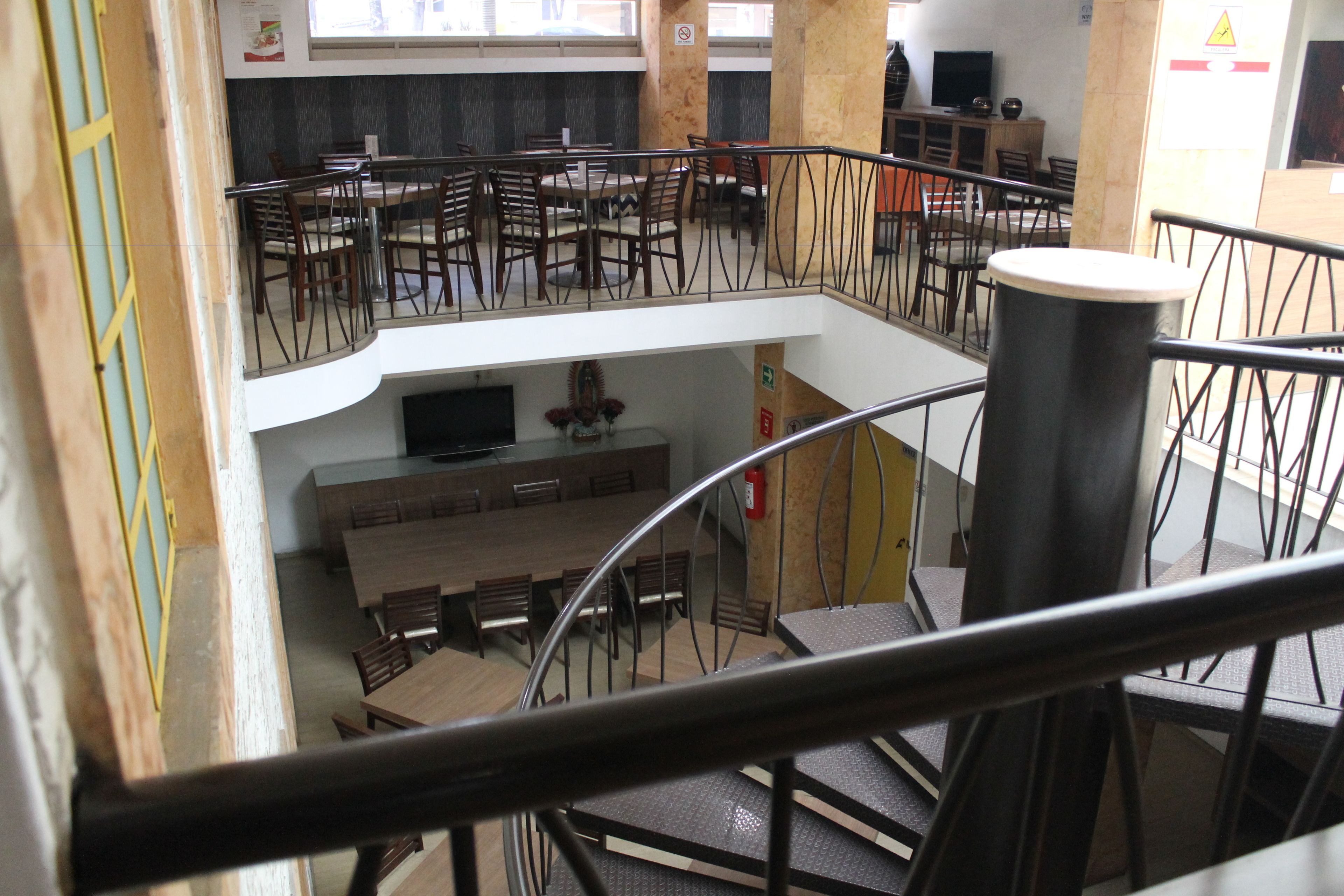 A multi-level dining area with wooden tables and chairs, a central TV, and a staircase.