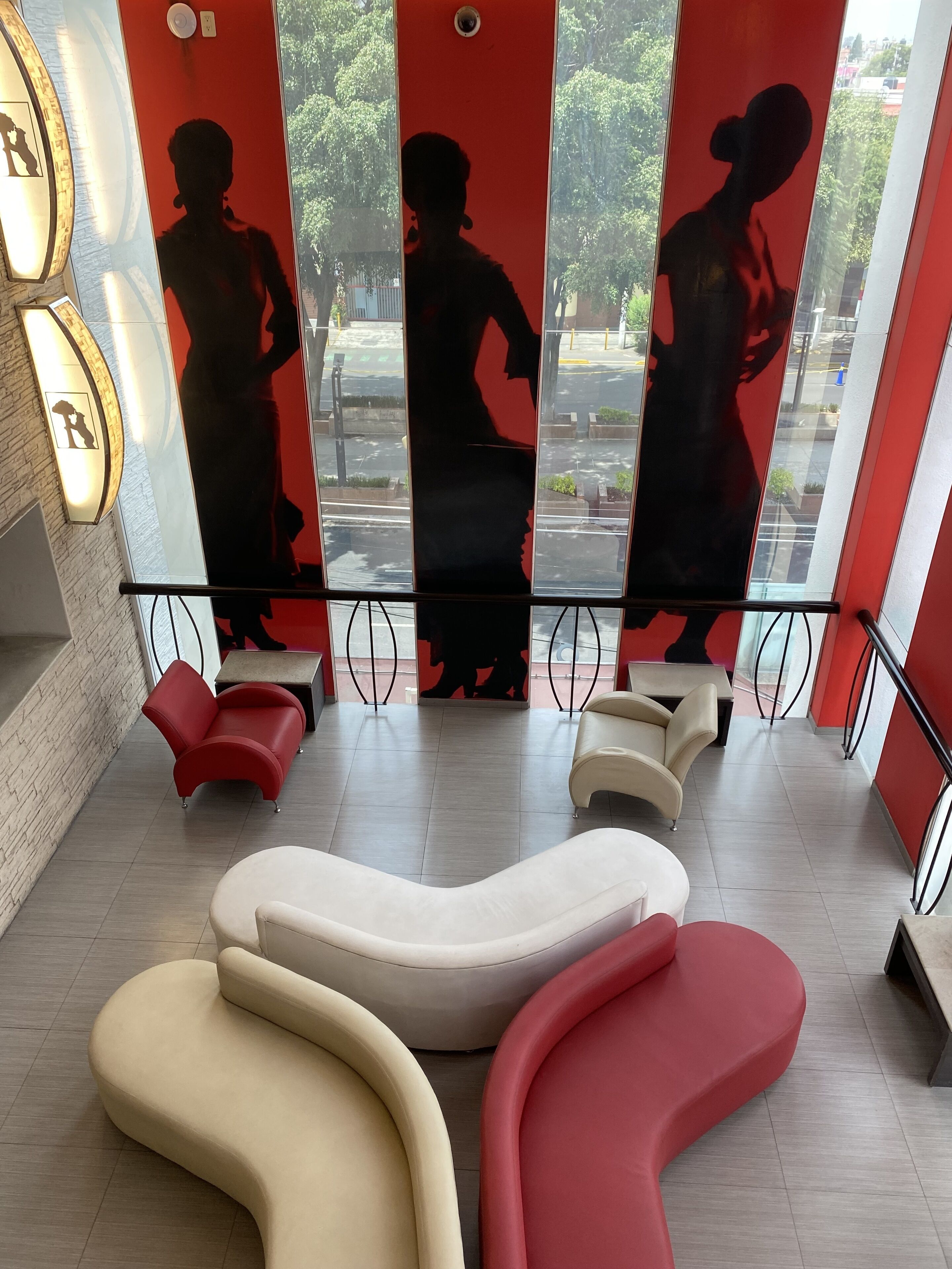 A modern interior with red and beige seating, a glass wall with a view of the street, and a brick wall with a light fixture.