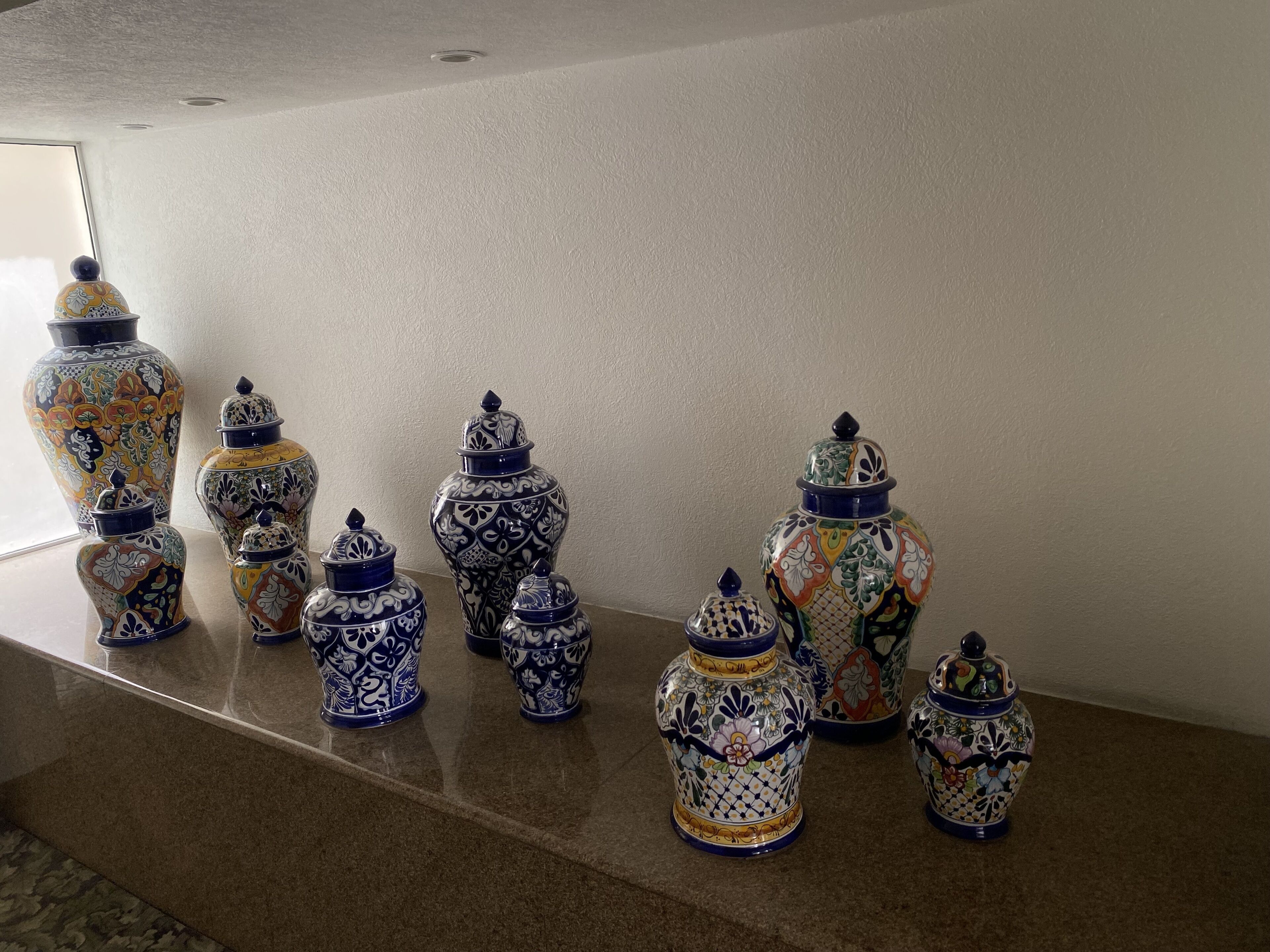 Una hilera de jarrones de cerámica decorados sobre un repisa de mármol frente a una pared lisa.