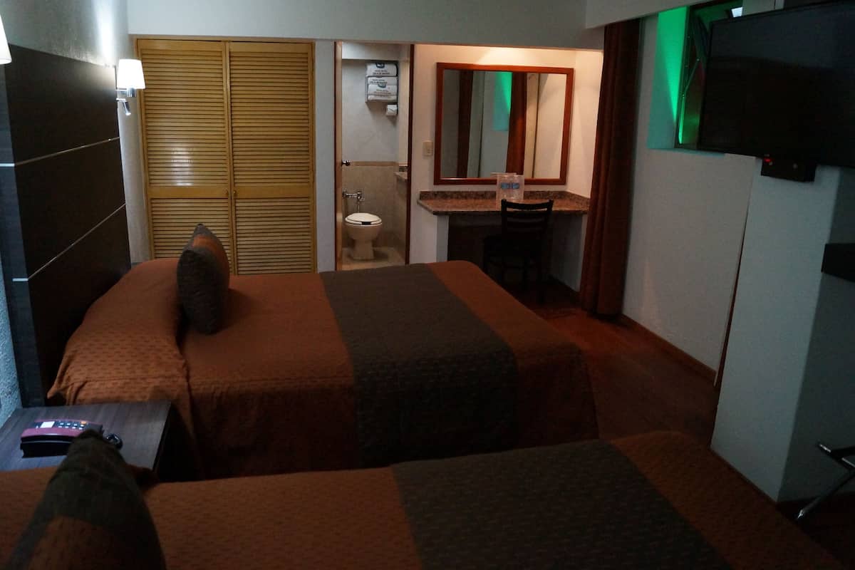 A hotel room with two beds, a desk, a chair, a television, and a bathroom.