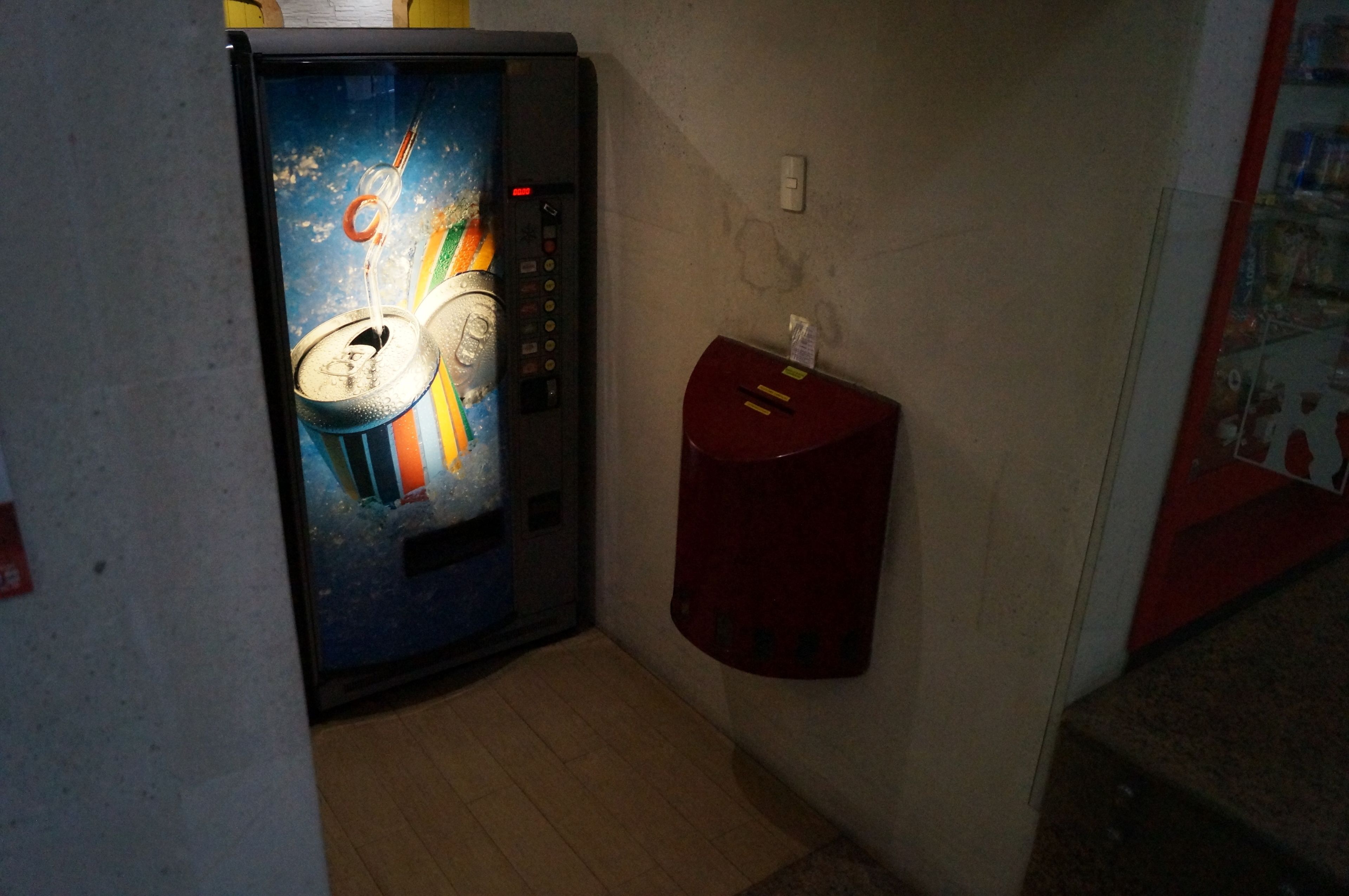 A narrow hallway with a vending machine and a fire alarm box on the wall.