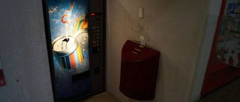 A narrow hallway with a vending machine and a fire alarm box on the wall.