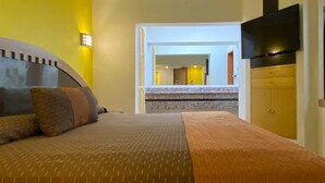 Habitación de hotel con una cama, un televisor y un baño visible a través de una puerta abierta.