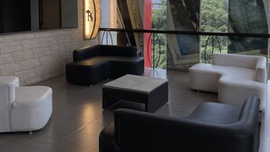 Un área de descanso moderna con pared de piedra, sofás blancos y negros, una mesa de centro y ventanas amplias con vistas a la ciudad.