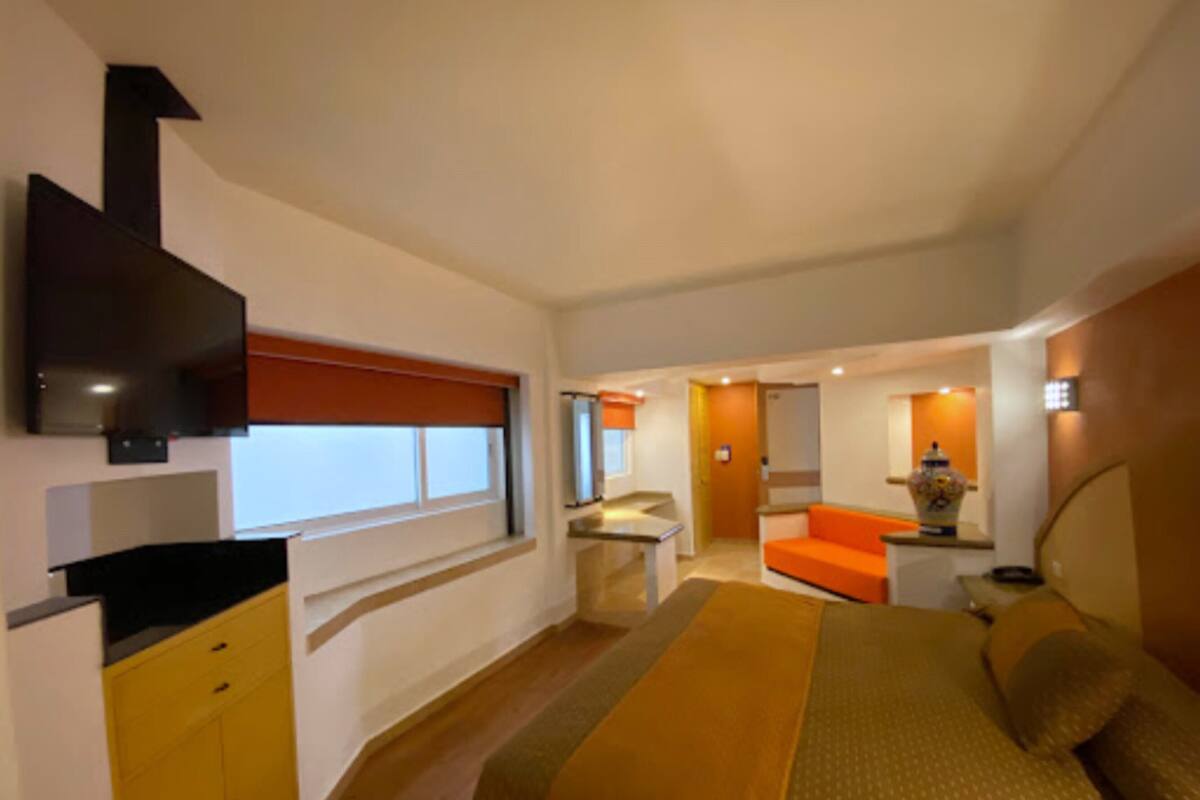 A modern hotel room with a bed, a desk, a chair, and a television.