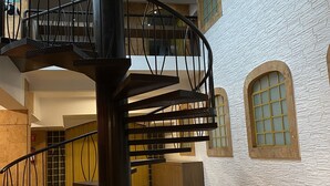 Una escalera de caracol con barandilla de metal negro en un edificio de paredes de ladrillo blanco y ventanas de arco.