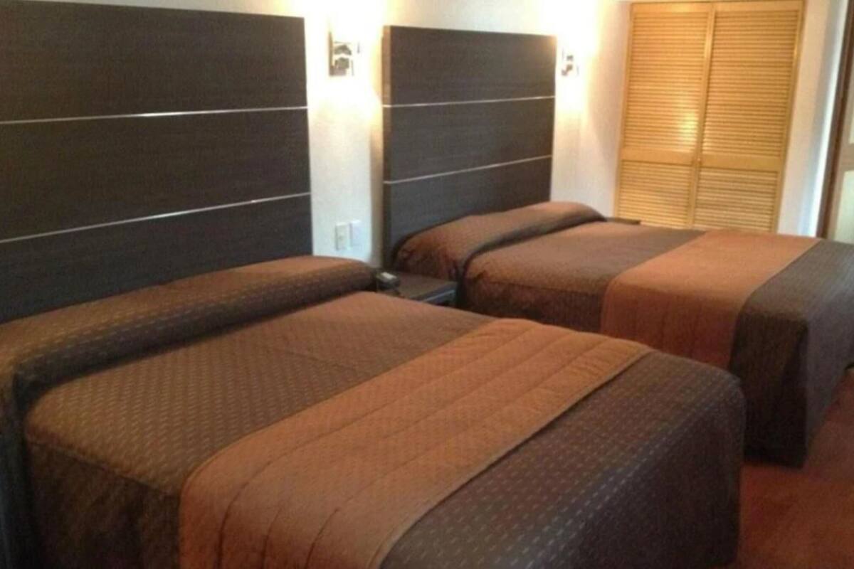 A hotel room with three beds, each with a headboard and a brown bedspread.
