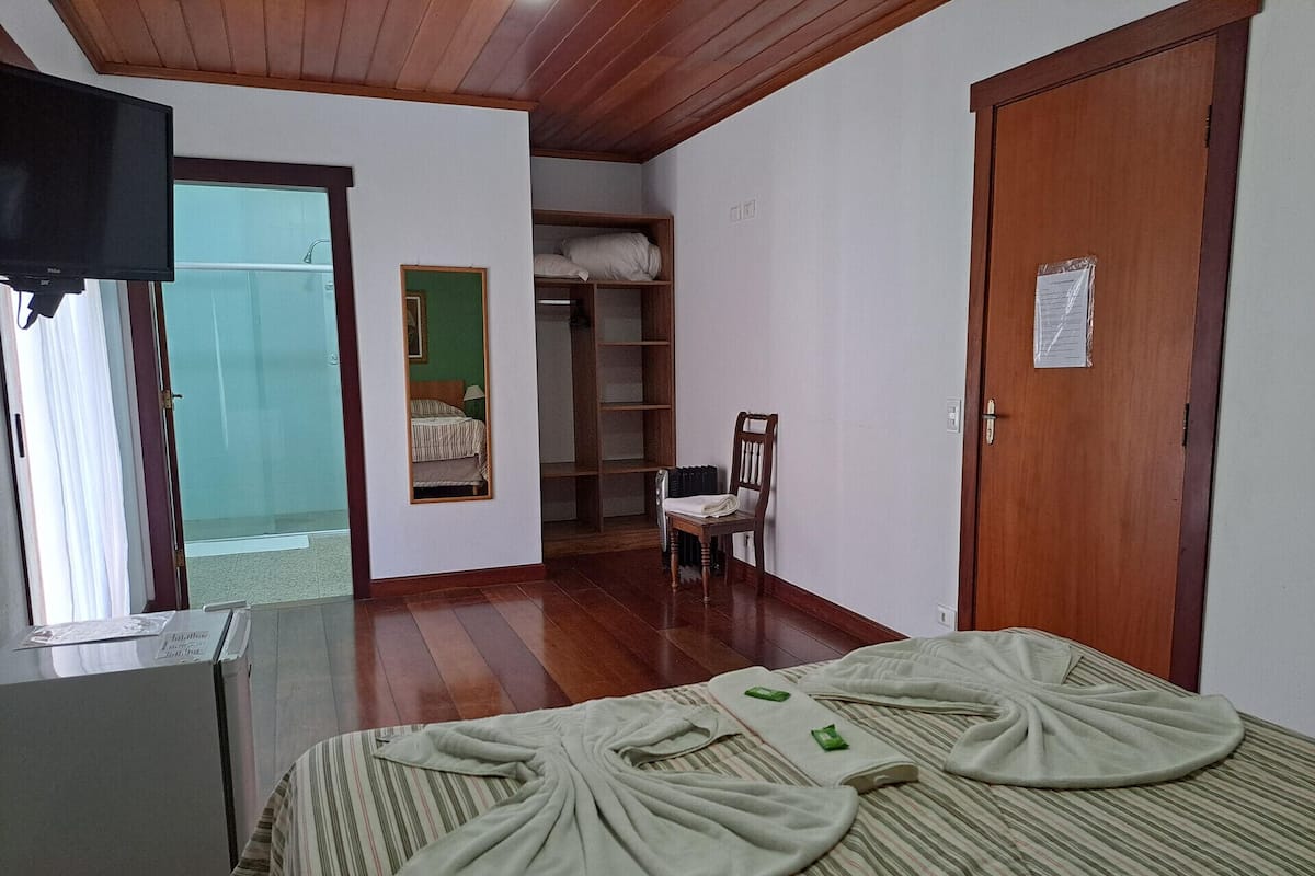 A bedroom with a bed, a chair, a wooden wardrobe, a television, and a window.