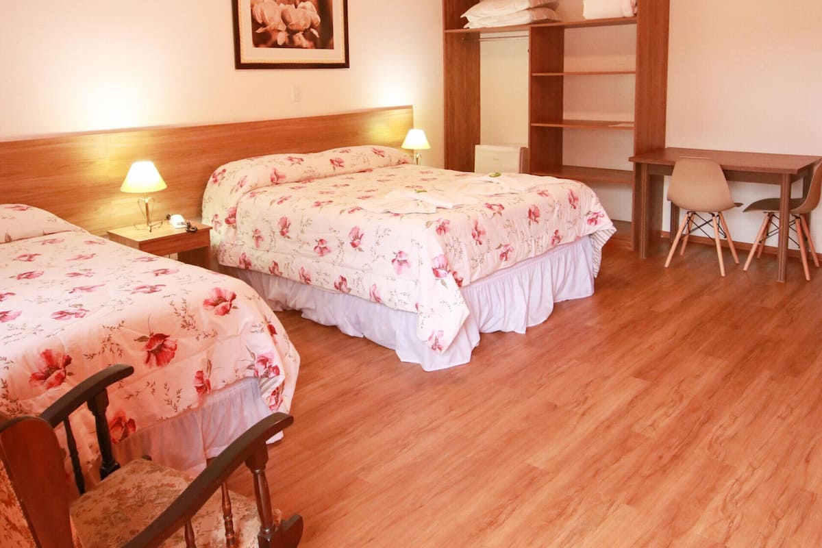 A room with two beds, a desk, and a chair. There is a mirror and a shelf with folded towels.