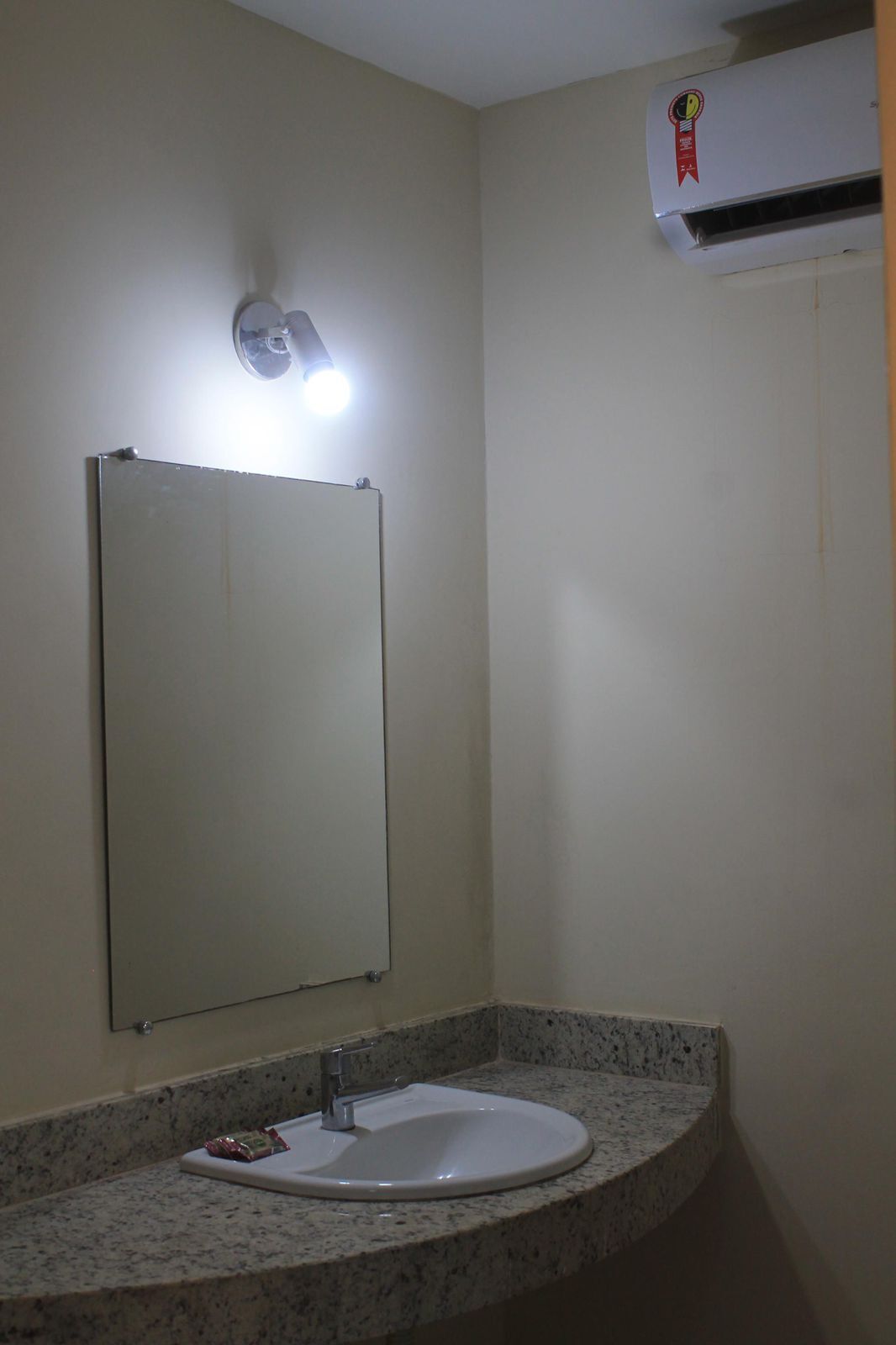 Un baño con un lavamanos blanco, un espejo y un aire acondicionado de pared.