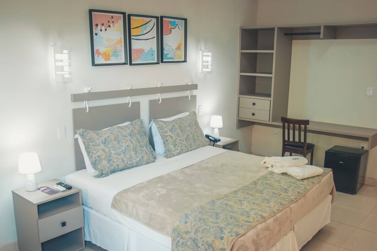A neatly arranged hotel room with a bed, bedside tables, a desk, and a wardrobe.