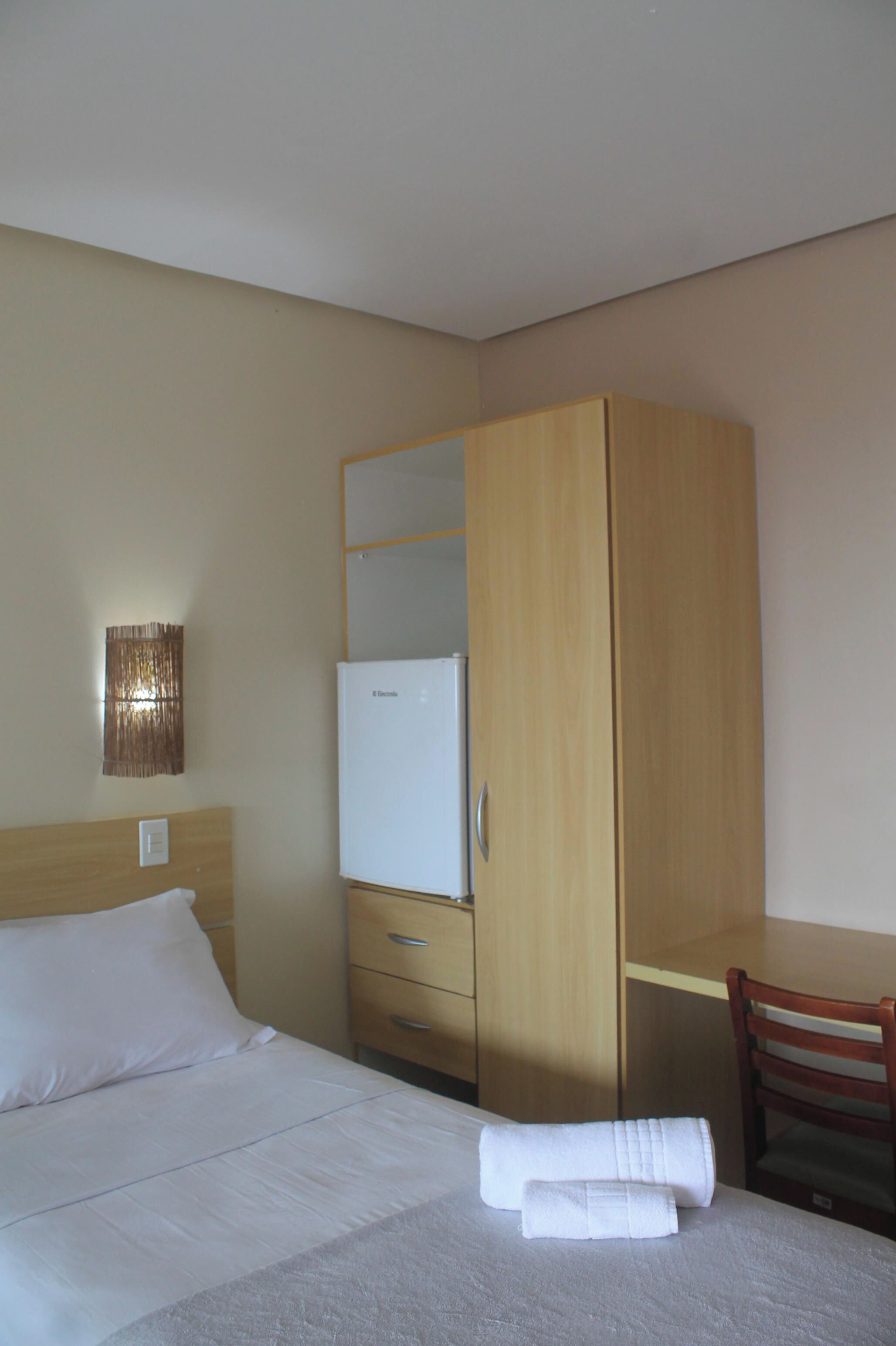 A hotel room with a bed, a wooden wardrobe, a desk, and a chair.