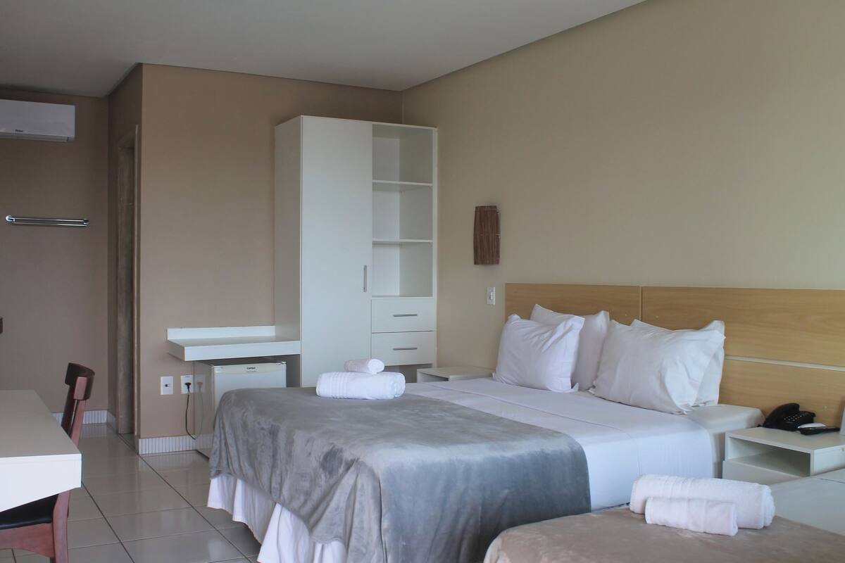 A hotel room with a bed, bedside tables, a wardrobe, a desk, and a chair.