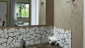 A bathroom with a granite countertop sink, a white toilet, a mirror with a mosaic backsplash, and a ceiling-mounted air conditioner.