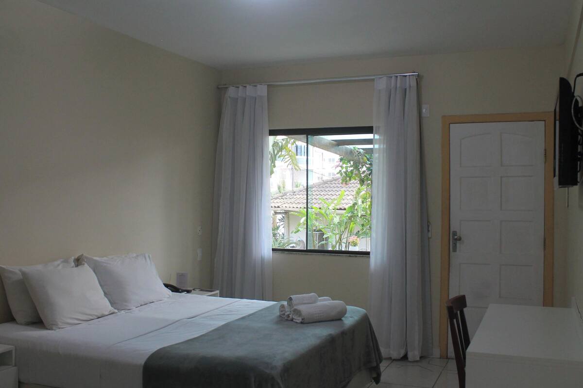 A hotel room with a bed, a table, and a window with curtains.