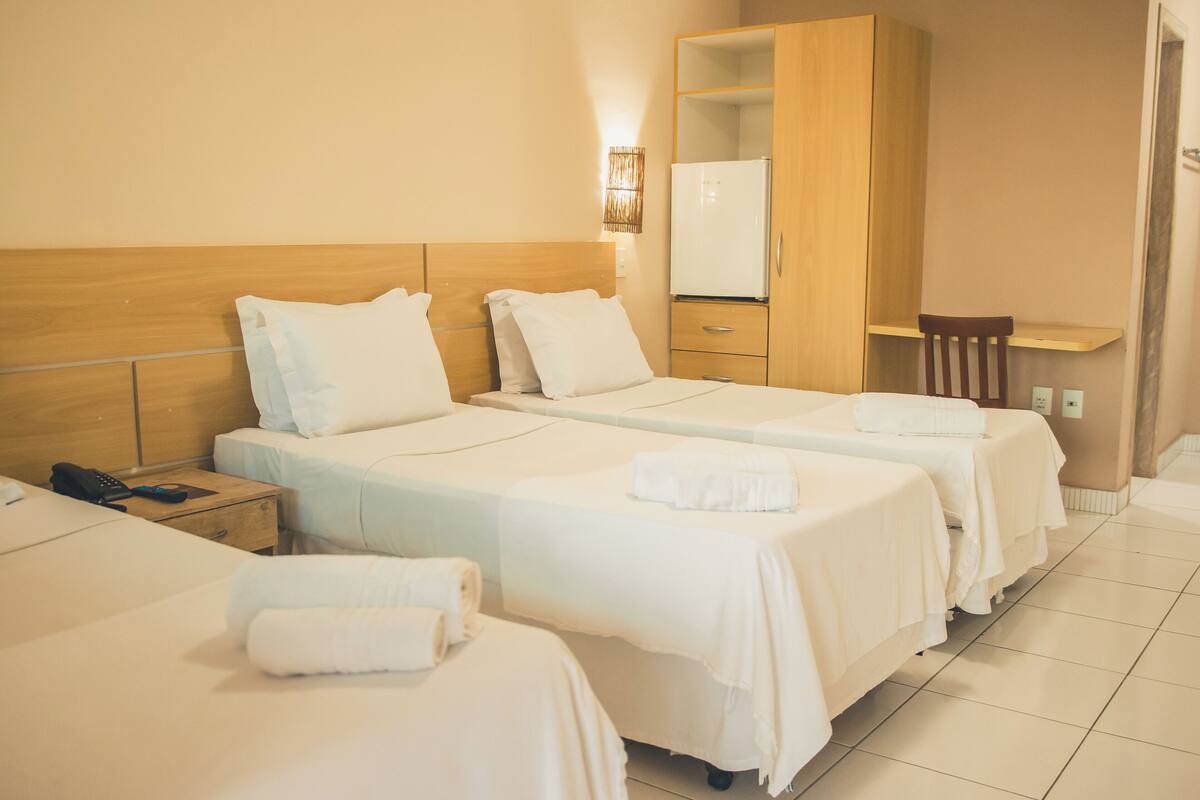 A hotel room with three beds, a wooden wardrobe, a desk, and a chair.
