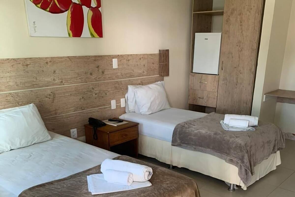 A hotel room with two beds, a wooden headboard, a wardrobe, and a painting on the wall.