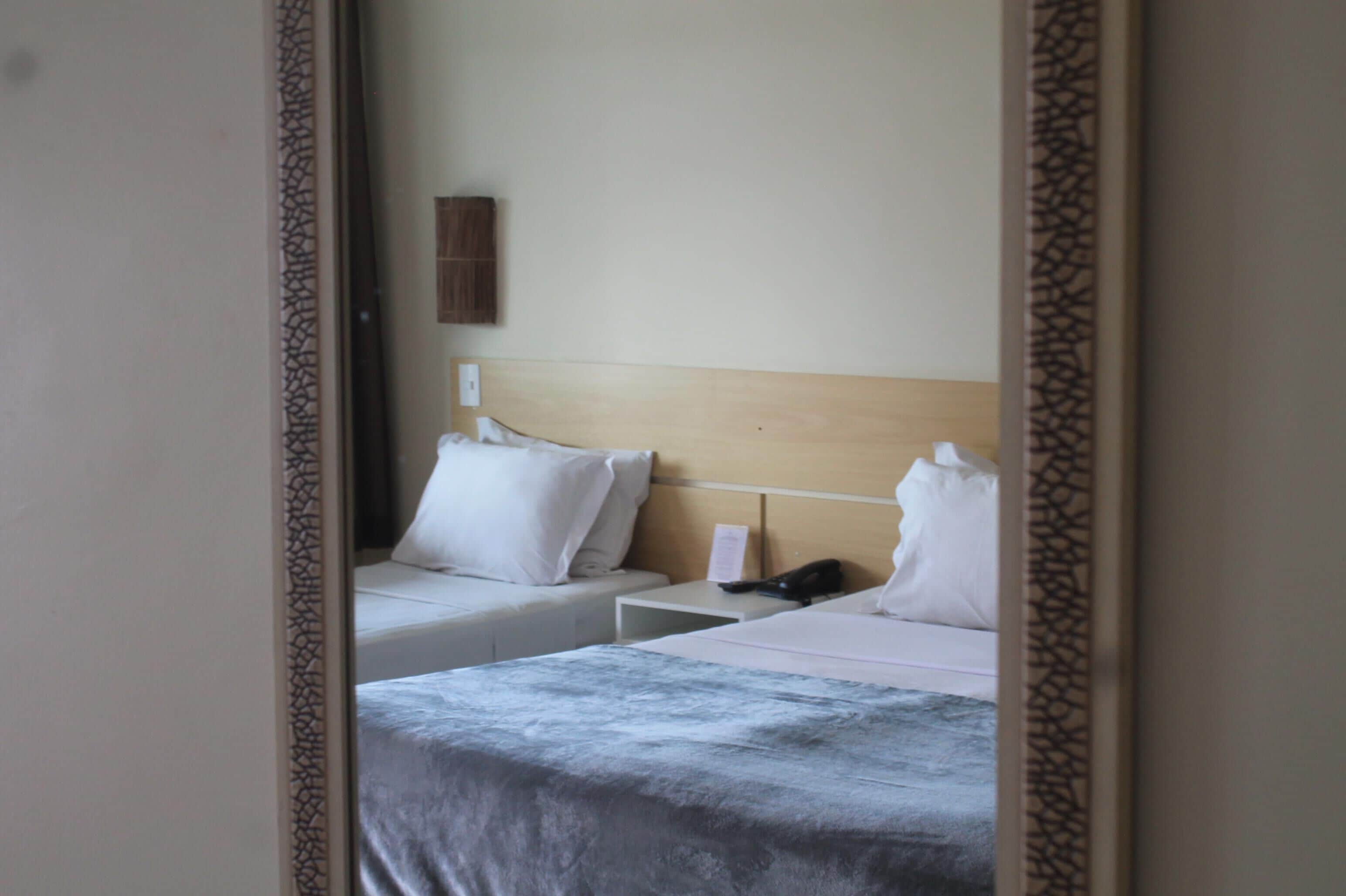Habitación de hotel con dos camas, cabecera de madera, mesita de noche con teléfono y aplique de pared.