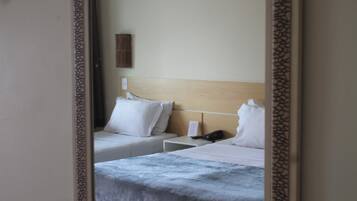 Habitación de hotel con dos camas, cabecera de madera, mesita de noche con teléfono y aplique de pared.