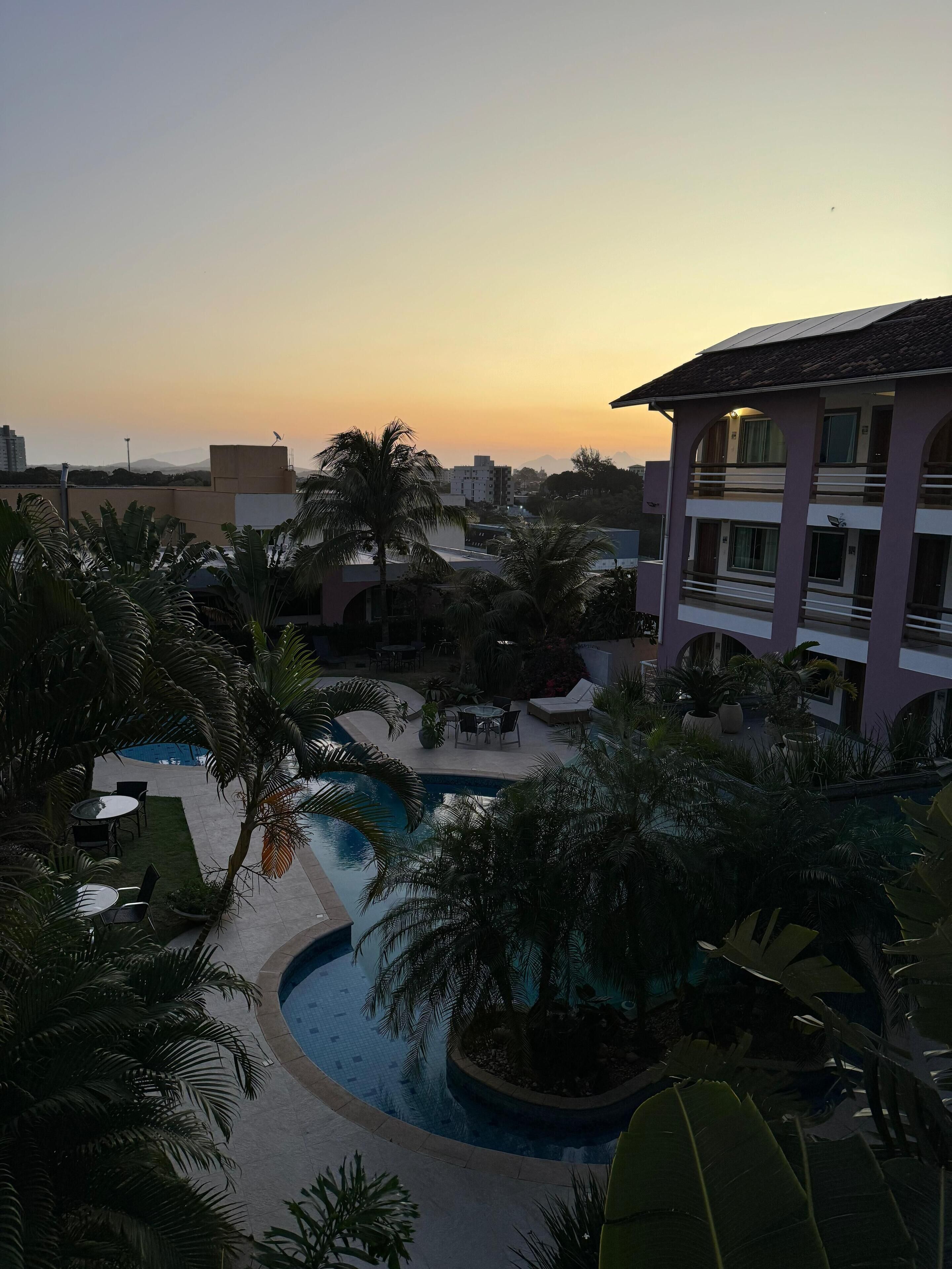 Ein Resort mit einem Swimmingpool, umgeben von Palmen und Blick auf einen Sonnenuntergang.
