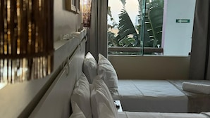 A hotel room with a large bed, a bedside table, a lamp, and a window with a view of greenery outside.