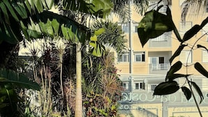 A garden with various plants and flowers, a pathway with white pebbles, and a building in the background.