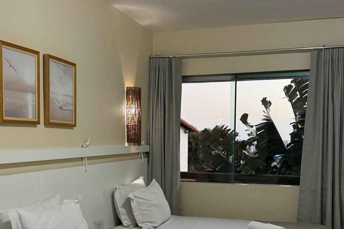 A hotel room with two beds, a large window with curtains, and a view of trees outside.