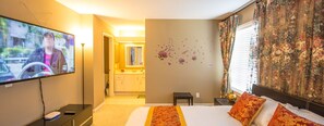 A hotel room with a bed, a TV, a desk, and a bathroom visible through an open door.