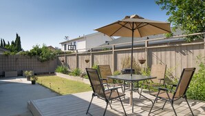 An outdoor patio with a table and chairs, a wooden deck, and a wooden fence. - Sunny and Elegant Villa (Newark)