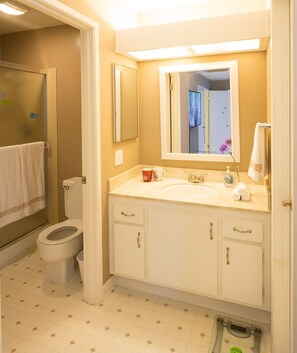 A bathroom with a toilet, sink, and mirror. There are towels and toiletries on the sink counter.