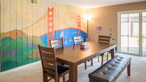A dining area with a wooden table, chairs, and a bench. A colorful mural of the Golden Gate Bridge is on the wall. - Sunny and Elegant Villa (Newark)
