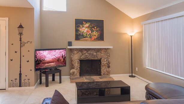 A living room with a stone fireplace, a flat-screen TV, a red sofa, and a floor lamp. - Sunny and Elegant Villa (Newark)