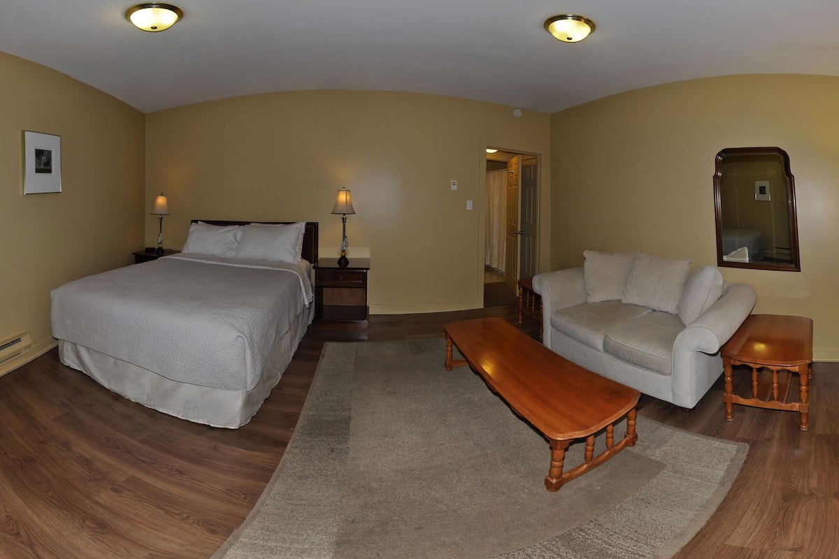 A hotel room with a bed, a sofa, a wooden coffee table, a nightstand, and a mirror.