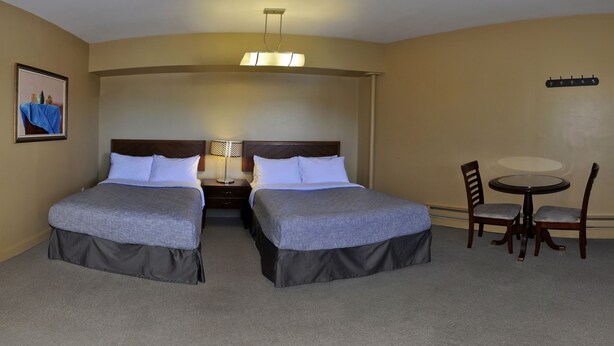 A hotel room with two beds, a nightstand, a table with chairs, a framed picture on the wall, and a ceiling light fixture. - Bond Guest House (St. John's)