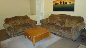 A living room with two patterned sofas, a wooden coffee table, and a painting on the wall. - Bond Guest House (St. John's)