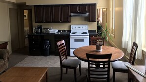 A compact kitchen with dark wooden cabinets, a white stove, and a dining area with a round table and four chairs. - Bond Guest House (St. John's)