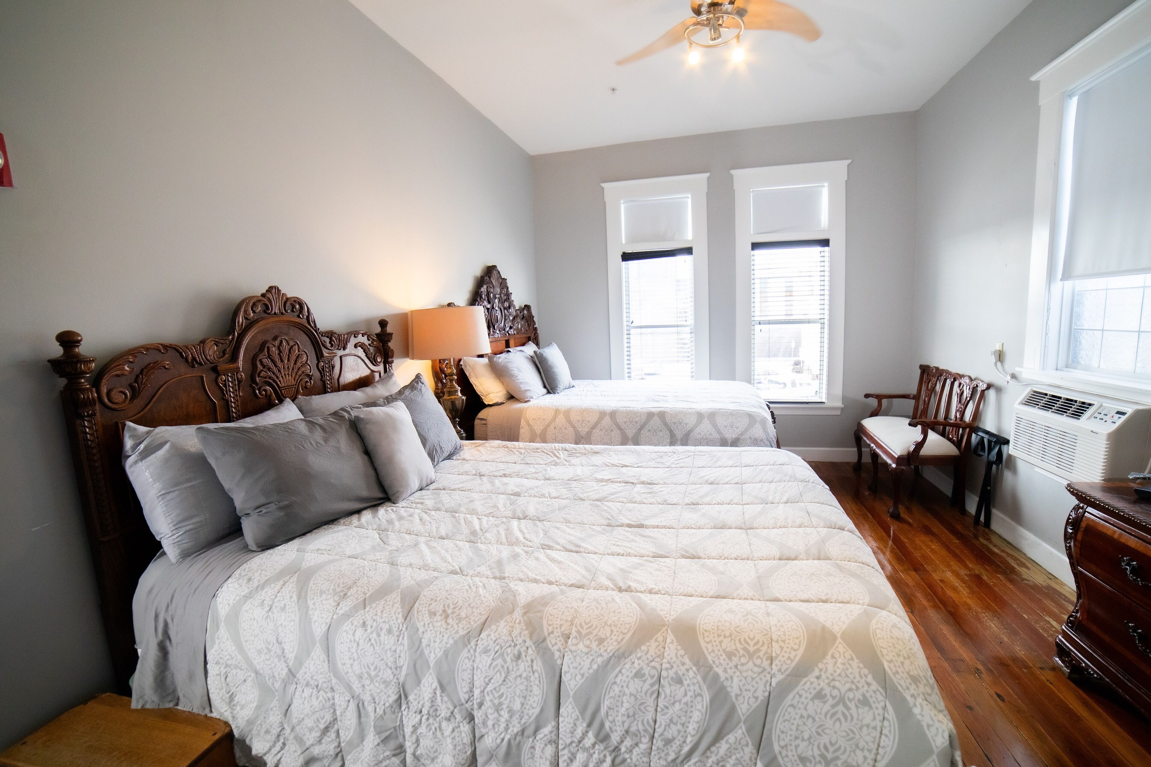 A bedroom with two beds, a wooden headboard, a nightstand, a chair, and a window with blinds.