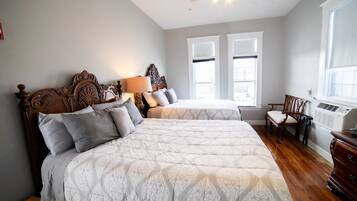 A bedroom with two beds, a wooden headboard, a nightstand, a chair, and a window with blinds.